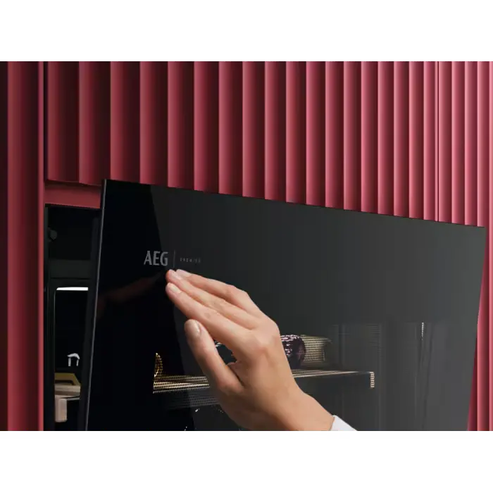 Hand opening a black AEG wine fridge oven against a red textured wall.